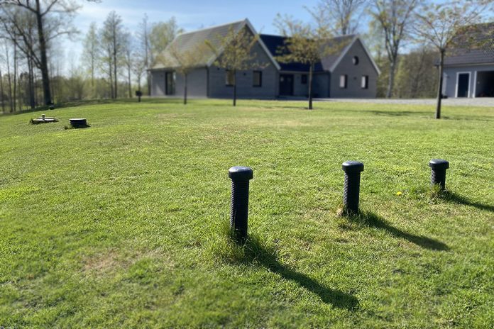 infiltrationsanläggning med tre luftningsrör på grön gräsmatta framför grått hus