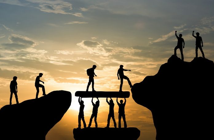 En grupp människor hjälps åt att klättra mot toppen. En grupp står och lyfter stor sten åt andra att gå på.