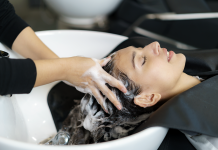 kvinna ligger bakåtlutad i frisörs tvättställ, händer masserar in lödder i hennes blöta hår.