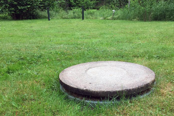 stort grått lock i betong i marknivå på grön gräsmatta.