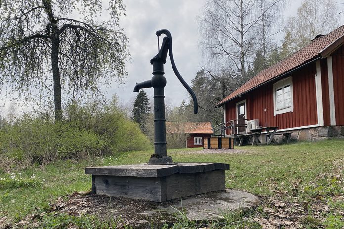 gammal svart dricksvattenpump. i bakgrunden röda stugor.