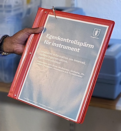 Röd pärm med texten egenkontrollpärm för instrument.