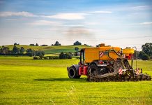 Traktor sprider flytgödsel på gräs. Gröna kullar i bakgrunden.