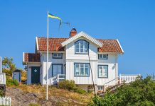 Vitt trähus på klippmark, blå himmel och solen lyser.