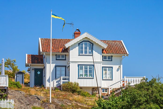 Vitt trähus på klippmark, blå himmel och solen lyser.