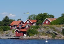 Röda hus med vita knutar, på klippa vid vatten.