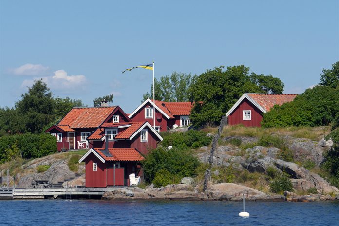 Röda hus med vita knutar, på klippa vid vatten.