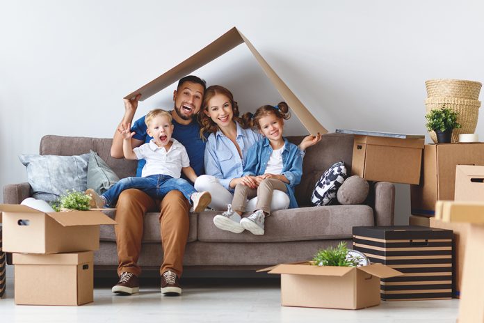 Mamma, pappa och två barn sitter i soffa omgivna av flyttkartonger.