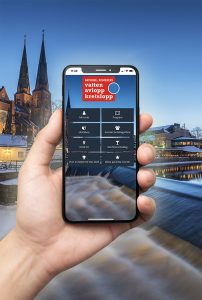 En hand som håller en mobil som visar eventappen för VAK 2025 med Uppsala domkyrka i bakgrunden.