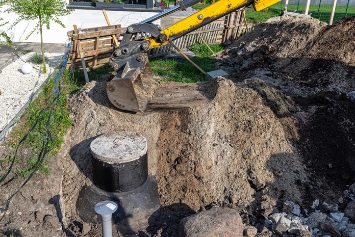 grävmaskin gräver ner en tank för enskilt avlopp i trädgård.