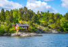 Grönskande ö med liten röd stuga på klipphäll vid vatten.