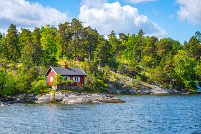 Grönskande ö med liten röd stuga på klipphäll vid vatten.