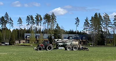 traktor på grönt fält framför radhus.