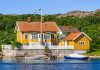 Gult trähus på klippa, gröna buskar runtomkring.
