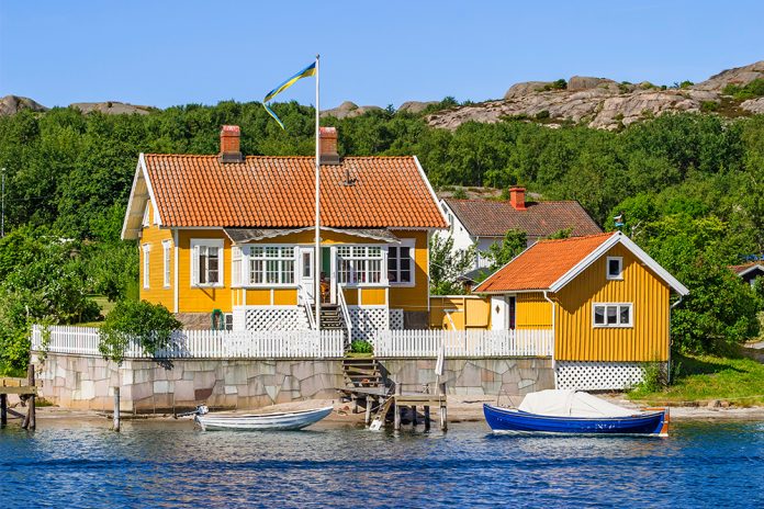 Gult trähus på klippa, gröna buskar runtomkring.