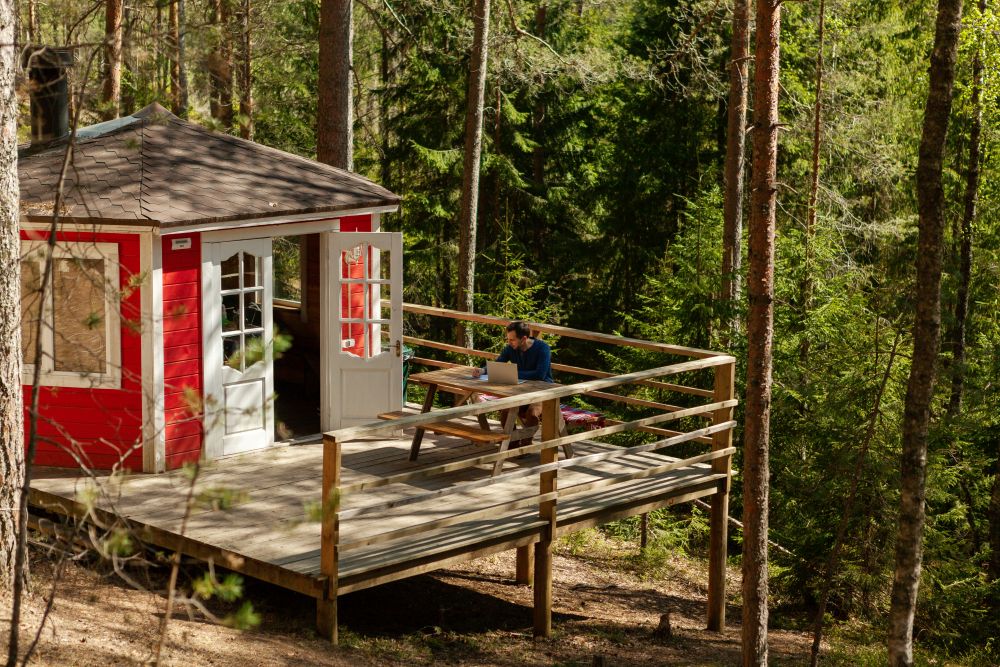 Liten stuga med terass i sluttning bland barrträden.