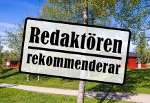Skylt med texten redaktören rekommenderar. Bakom finns grönt gräs, en björk och röda stugor.