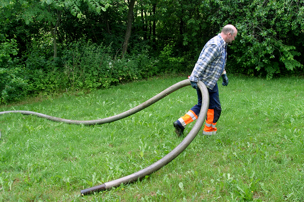 Man drar en tjock slang &ouml;ver en gr&ouml;n gr&auml;smatta
