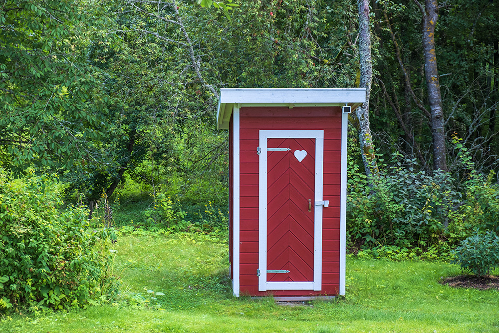 Litet tr&auml;hus, r&ouml;tt med vita knutar och ett hj&auml;rta p&aring; d&ouml;rren, i en gr&ouml;n tr&auml;dg&aring;rd.