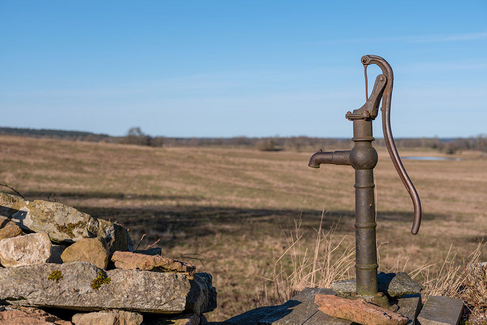Brun gammal vattenpump i jordbrukslandskap.